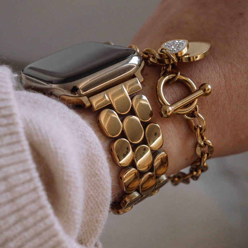 Close-up of a gold stainless steel Apple Watch band on a wrist with charm bracelets.